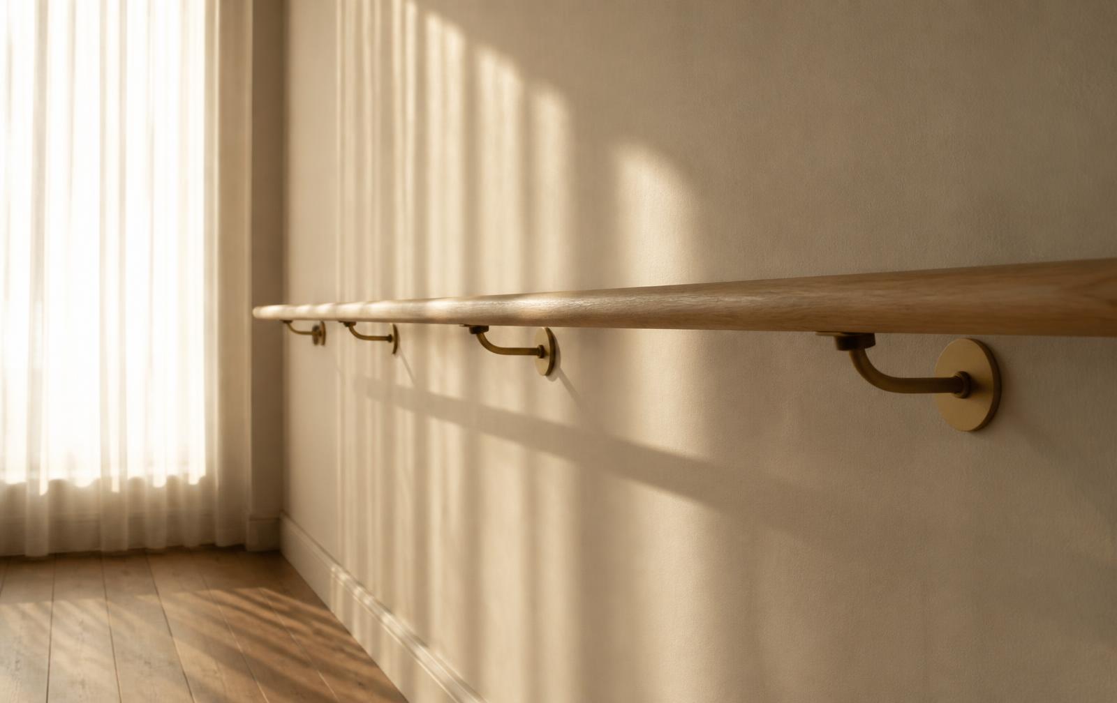 Wooden barre rail with sunlight across a cream studio wall